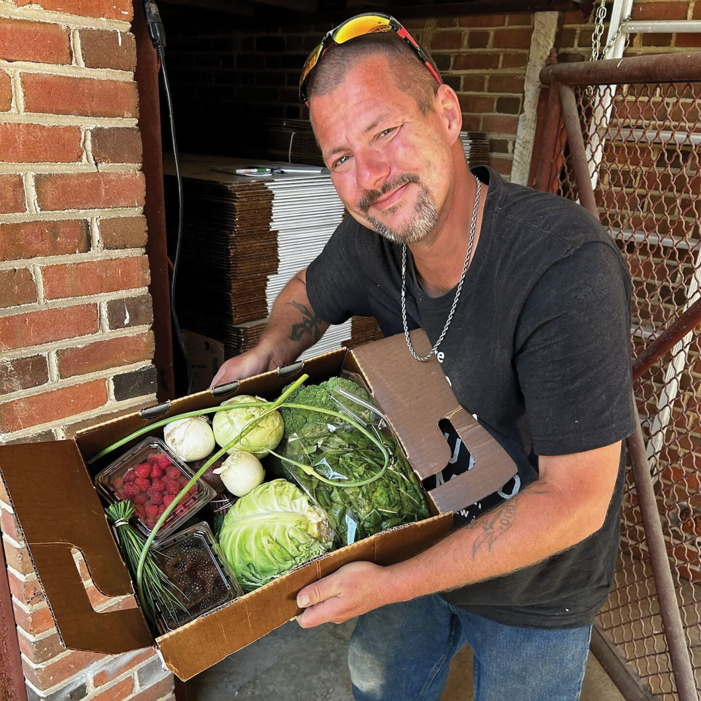 A man holds a box of fruit and vegetables, including lettuce, broccoli and raspberries.